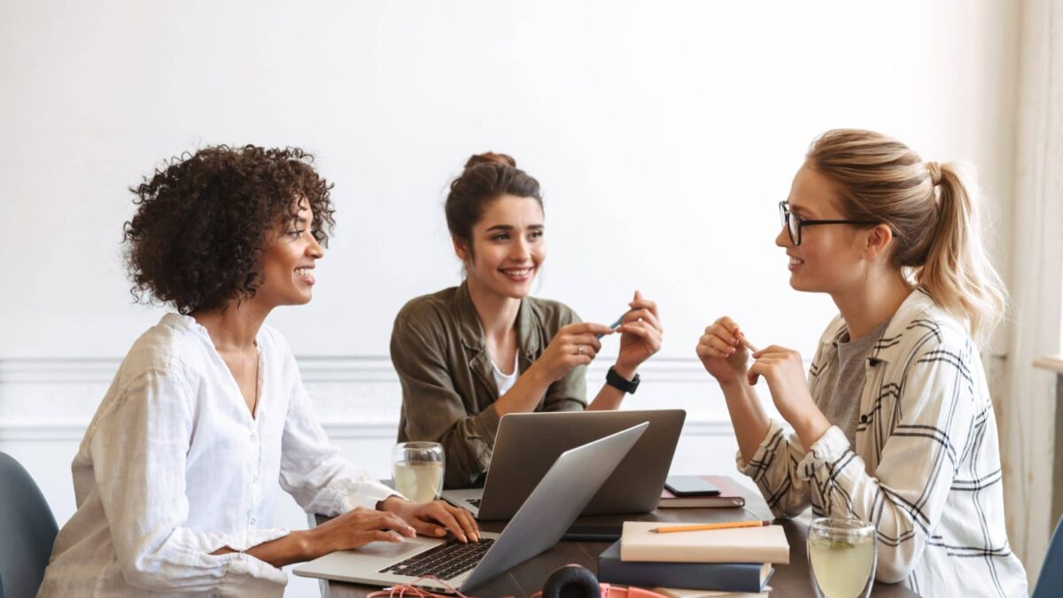 Três líderes mulheres em uma reunião, discutindo estratégias de comunicação eficaz no ambiente de trabalho."
