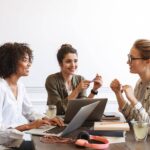 Três líderes mulheres em uma reunião, discutindo estratégias de comunicação eficaz no ambiente de trabalho."