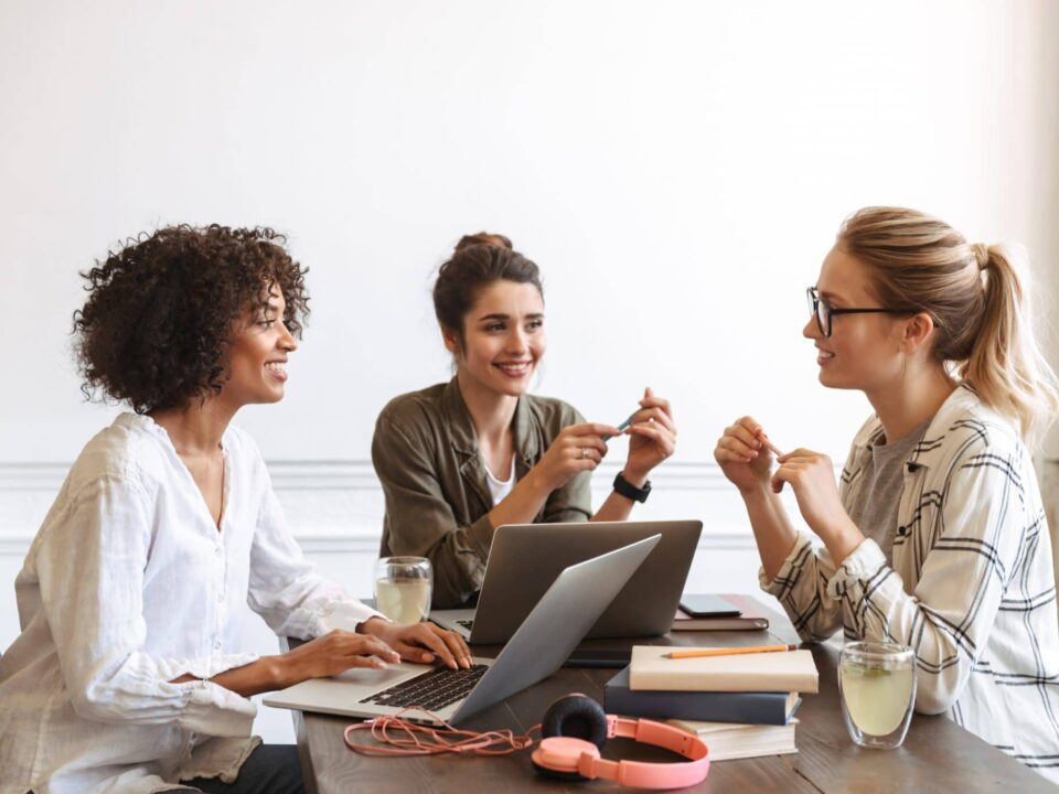Três líderes mulheres em uma reunião, discutindo estratégias de comunicação eficaz no ambiente de trabalho."